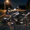 Se observa una motocicleta color negra, está destrozada y en una carretera; es de noche.