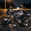 Se observa una motocicleta color negra, está destrozada y en una carretera; es de noche.