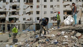 Rescatistas y hombres de Venezuela realizando labores de rescate en una pila de escombros con palas y un edificio destruido en el fondo