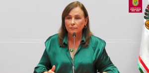 Mujer vestida con blusa verde hablando ante un micrófono.