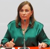 Mujer vestida con blusa verde hablando ante un micrófono.
