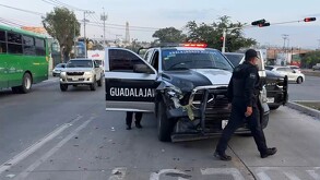 Patrulla de la Policía de Guadalajara atravesada en la calle con las puertas abiertas e impactada de la parte del frente y un policía caminando frente a ella