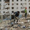 Rescatistas y hombres de Venezuela realizando labores de rescate en una pila de escombros con palas y un edificio destruido en el fondo
