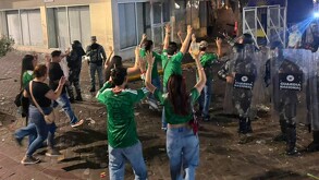 Hombres y mujeres con playeras de la Selección Mexicana vistos de espaldas con las manos en alto caminando hacia policías de la Guardia Nacional en Guadalajara