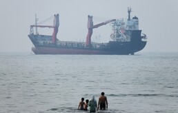 Varias personas se meten en el agua en la orilla mientras un carguero aparece fondeado en el estrecho de Ormuz, ante la costa de Bandar Abbas, Irán