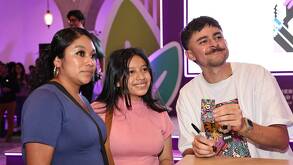Una mujer y una joven con el ilustrador Kevin Cuevas sosteniendo la tarjeta de movilidad conmemorativa