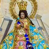 Figura de la Virgen de Zapopan protegida con una estructura de plástico reforzada con candados delante de un fondo de un cielo amarillo