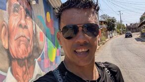 Hombre de gafas y playera negra hablando a una cámara en un día soleado.