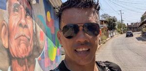 Hombre de gafas y playera negra hablando a una cámara en un día soleado.