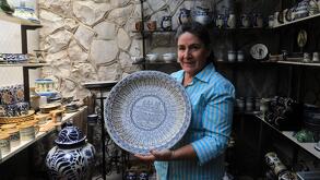 una mujer sostiene un plato de talavera dentro de un taller en puebla