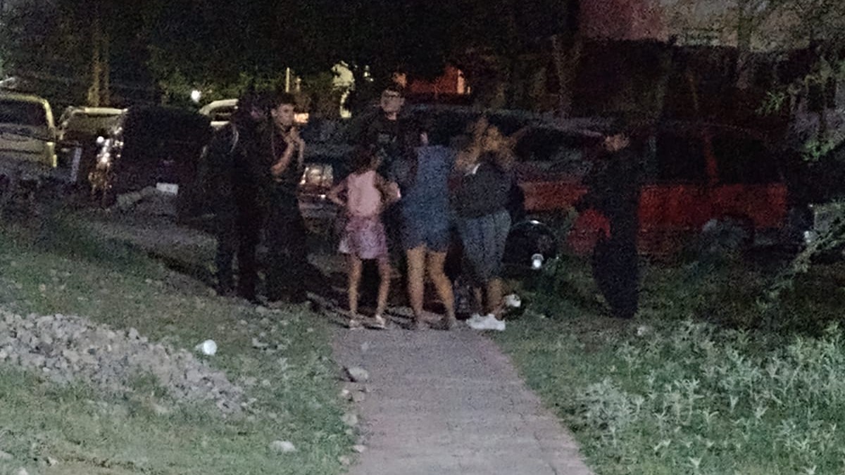 VARIAS PERSONAS PARADAS EN LA CALLE A OSCURAS RODEADAS DE ÁRBOLES