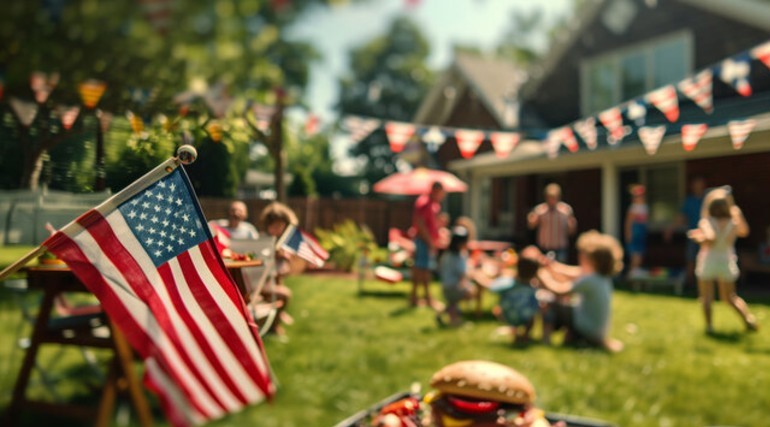 Vista desenfocada de una fiesta familiar por el Día de la Independencia de Estados Unidos en el patio de una casa con una bandera en primer plano