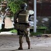 Militar del Ejército Mexicano visto de espaldas en la esquina de una calle con un poste, un árbol y una camioneta alrededor