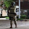 Militar del Ejército Mexicano visto de espaldas en la esquina de una calle con un poste, un árbol y una camioneta alrededor