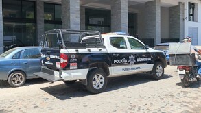 Patrulla de la Policía de Puerto Vallarta estacionada al exterior de un edificio de departamentos con autos y un motociclista alrededor