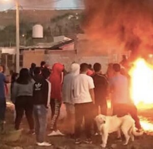 Pobladores reunidos frente a un vehículo incendiado en llamas.