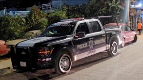 Vista lateral de noche de una patrulla de la Policía de Zapopan frente a unas plantas y con automóviles alrededor