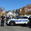 Patrullas y oficiales del Departamento de Policía de Nueva York desplegados en una calle acordonada con casas y árboles alrededor