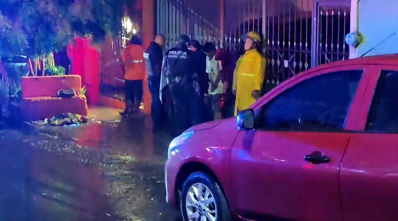 Policías de Guadalajara junto con elementos de Protección Civil y Bomberos atendiendo a dos hombres afuera de un domicilio bajo la lluvia