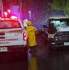 Camioneta de Protección Civil y Bomberos al lado de una patrulla de la Policía de Guadalajara con policías y un bombero parados bajo la lluvia