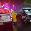 Camioneta de Protección Civil y Bomberos al lado de una patrulla de la Policía de Guadalajara con policías y un bombero parados bajo la lluvia