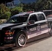 Vista lateral de noche de una patrulla de la Policía de Zapopan frente a unas plantas y con automóviles alrededor