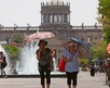 Mujeres mayores caminando son sombrillas para protegerse del sol en el centro de Guadalajara con el Hospicio Cabañas desenfocado en el fondo