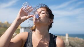 Una mujer con una camiseta negra bebiendo agua de una botella transparente