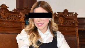 Se observa a una mujer sonriendo con ojos cubiertos y viste una camisa blanca y chaleco negro.