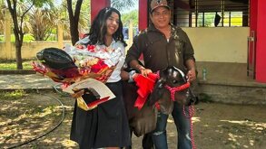 una joven estudiante y un hombre junto a un becerro en una ceramonia de graduación