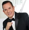 Benjamín Medrano Quezada sonriendo, vestido de traje y con la mano cerrada en puño delate de un fondo blanco