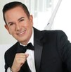 Benjamín Medrano Quezada sonriendo, vestido de traje y con la mano cerrada en puño delate de un fondo blanco