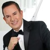 Benjamín Medrano Quezada sonriendo, vestido de traje y con la mano cerrada en puño delate de un fondo blanco