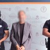 Un hombre siendo detenido, con la cara censurada con blur y con esposas en las manos en medio de dos policías de Jalisco con armas largas