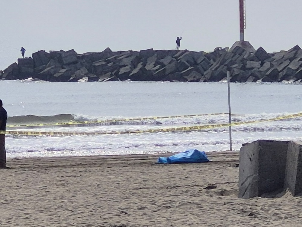 Cuerpo sin vida tapado con un traje especial en medio de la playa.
