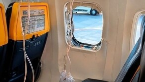 Ventanilla de un avión completamente rota con tubos de las máscara de oxígeno desplegadas en medio de los asientos