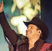 Hombre con traje mexicano y sombrero de charro sonriendo mientras levanta la mano ante un escenario.