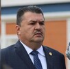 Julio Meza Gaona visto de perfil con el seño fruncido mientras viste de traje delante de un fondo naranaja