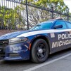 Vista del costado de una patrulla de la Policía de Michoacán estacionada al lado de un un parque con protección metálica