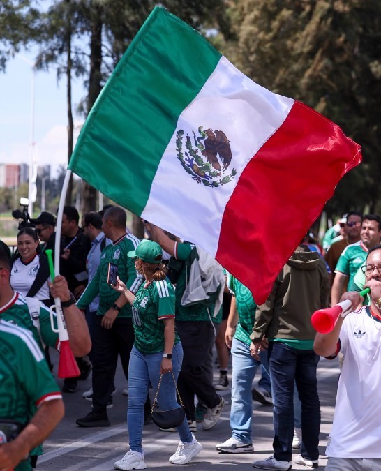 Aficionados caminando hacia el Estadio Akron con la playera de la Selección Mexicana y ondeando una bandera de México