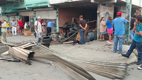 Se observan llantas y una fachada; hay varias personas paradas en la vía pública.