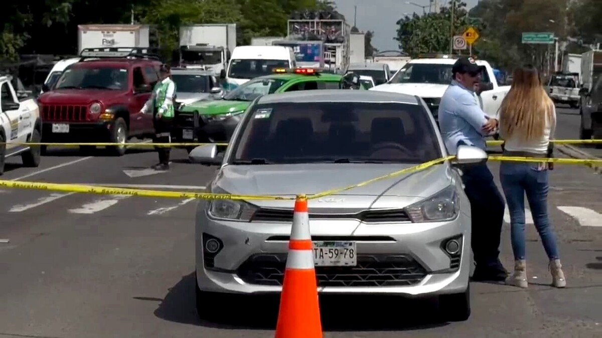 Vehículo tipo sedán de la marca Kia color gris dentro de un área acordonada por la Policía de Zapopan con una mujer y un hombre al lado