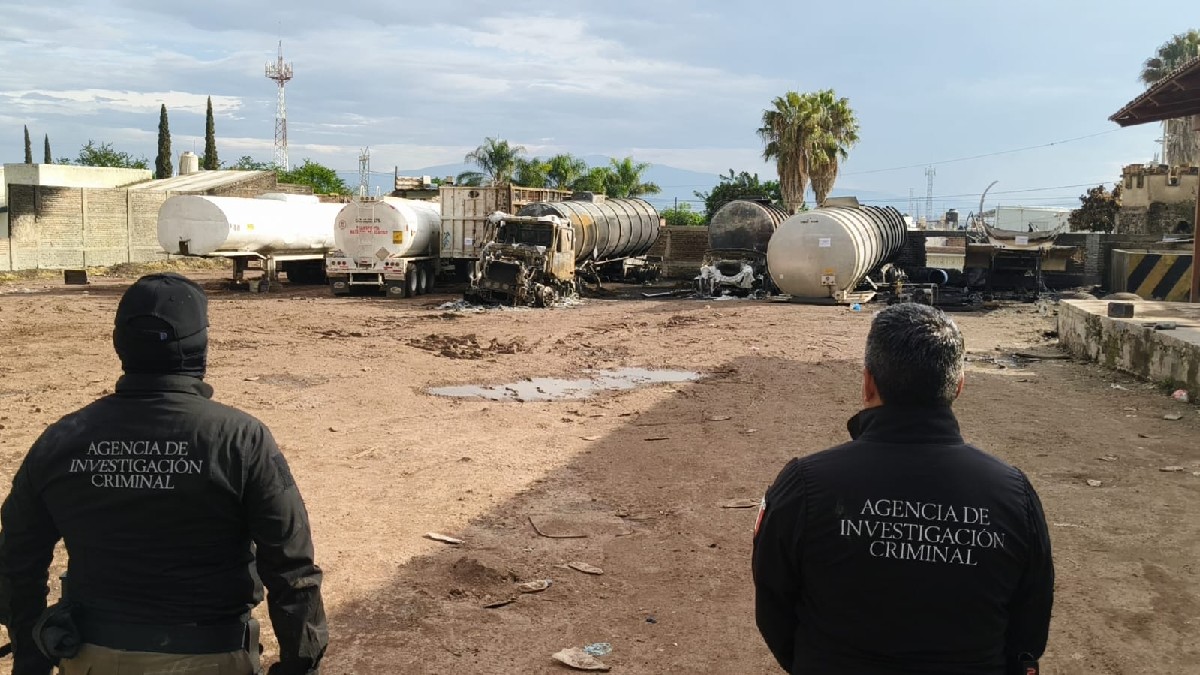 Agentes de la FGR vistos de espaldas parados delante de un terreno con pipas y camiones de gasolina quemados tras un incendio