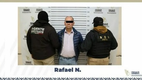 un hombre detenido con los ojos cubiertos custodiado por dos policías