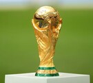 El trofeo de la Copa Mundial de la FIFA sobre una base blanca y al fondo una cancha de fútbol