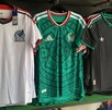 Tres playeras de la Selección Mexicana en colores blanco, verde y negro colgadas dentro de una tienda