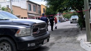 Se observa una cinta roja de precaución, varios autos estacionados sobre la vía pública.