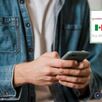 Vista del pecho hacia abajo de un hombre sosteniendo un teléfono celular con ambas manos y la imagen de una CURP a un lado