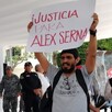 Hombre protestando en un evento oficial, mientras una mujer habla frente al micrófono.