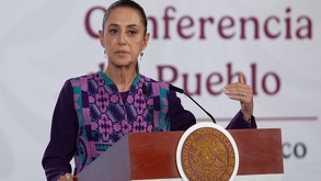 Mujer con cabello recogido y un traje colorido hablando ante un micrófono.